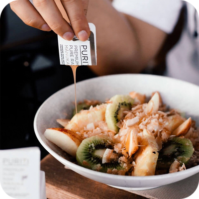 A person pouring novita SG Manuka honey into a bowl of food.