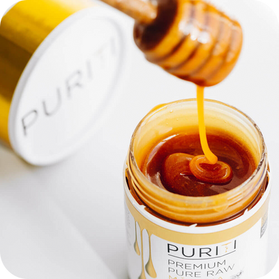 A person is pouring PURITI Premium Raw Manuka Honey UMF 18+ | MGO 700 from novita SG into a jar.