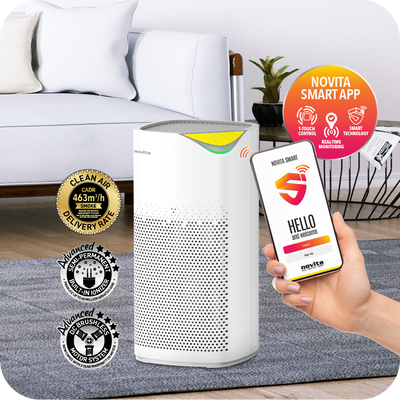 A person holding a smart phone next to a novita Air Purifier + Humidifier A2+H for communication and environmental wellness.