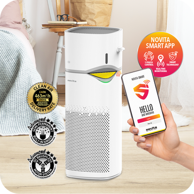 A person holding a smart phone next to a novita Air Purifier + Humidifier A2+H for an effective indoor air cleaning solution.