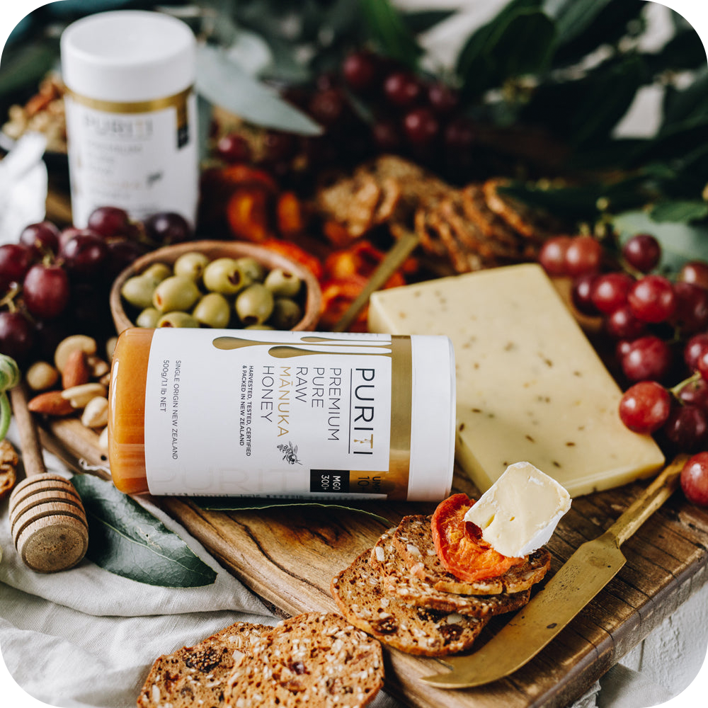 A cutting board with grapes, nuts, and a bottle of novita SG PURITI Premium Raw Manuka Honey UMF 10+ | MGO 300.